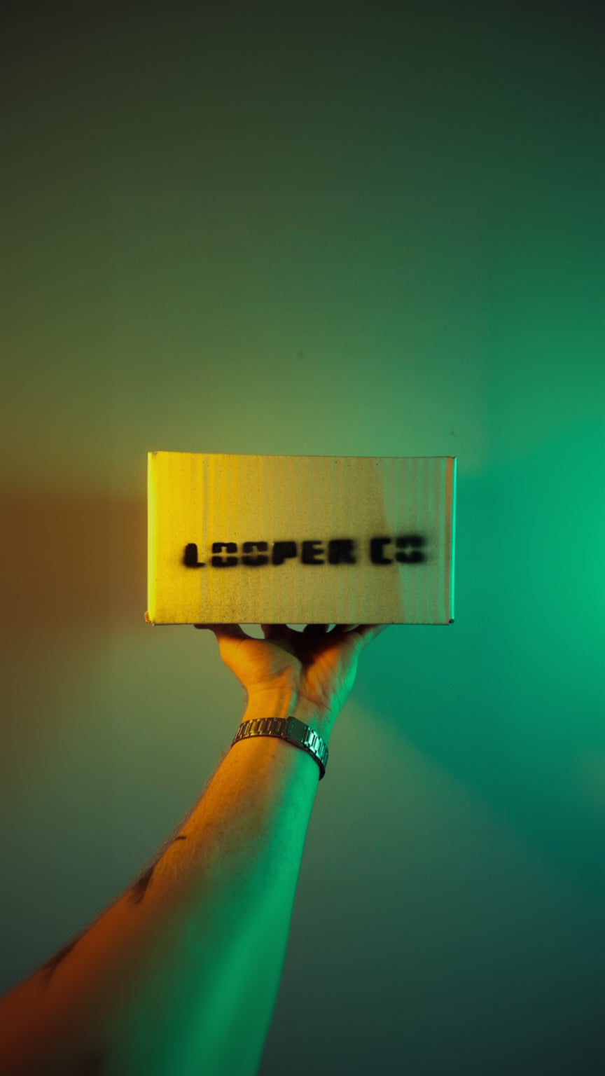 A hand holding a light-colored cardboard box with 'LOOPER CO' printed in black stencil-style lettering, set against a green-tinted background.